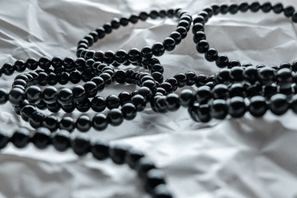 Nueve pulseras de bolas de obsidiana negra natural en primer plano sobre un fondo rugoso de color blanco