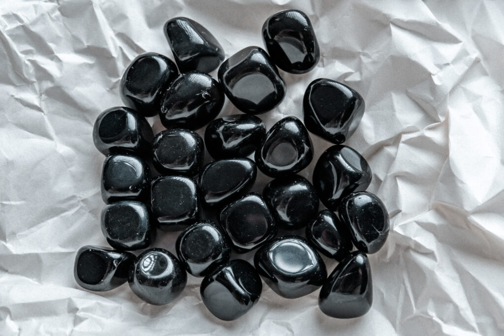 Rodados de obsidiana negra natural de diversas formas en primer plano sobre un fondo rugoso de color blanco